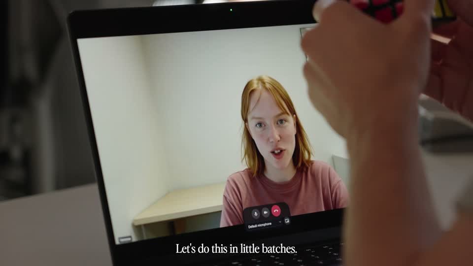 A laptop showing Vanessa, a woman in a pink shirt, while a man holds a Rubik's cube up to the camera.
